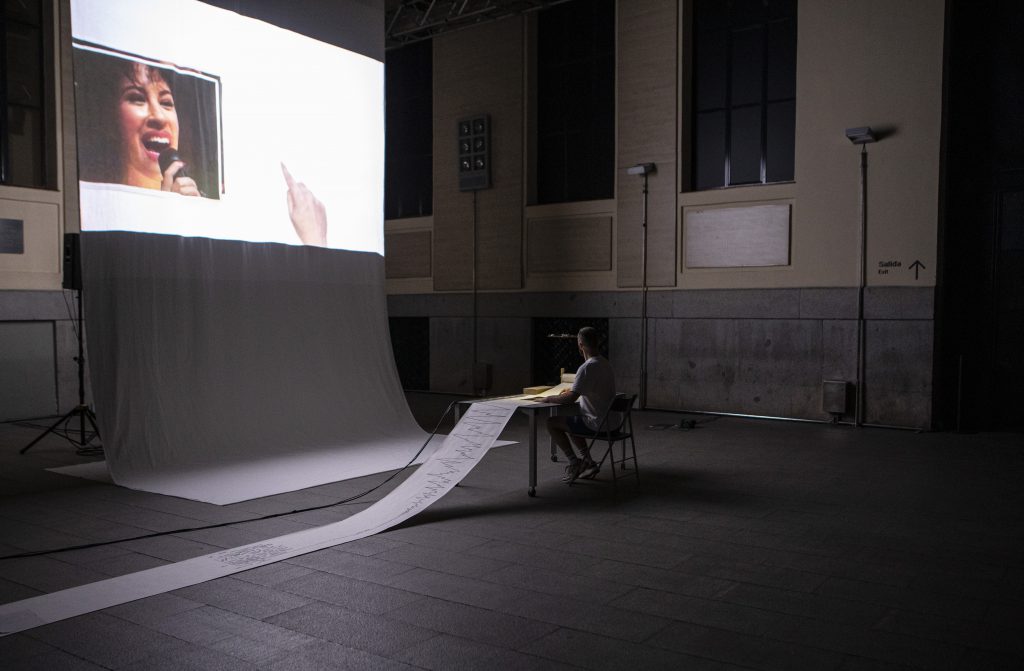 Óscar Bueno reading a score that is projected on a big and long white sheet