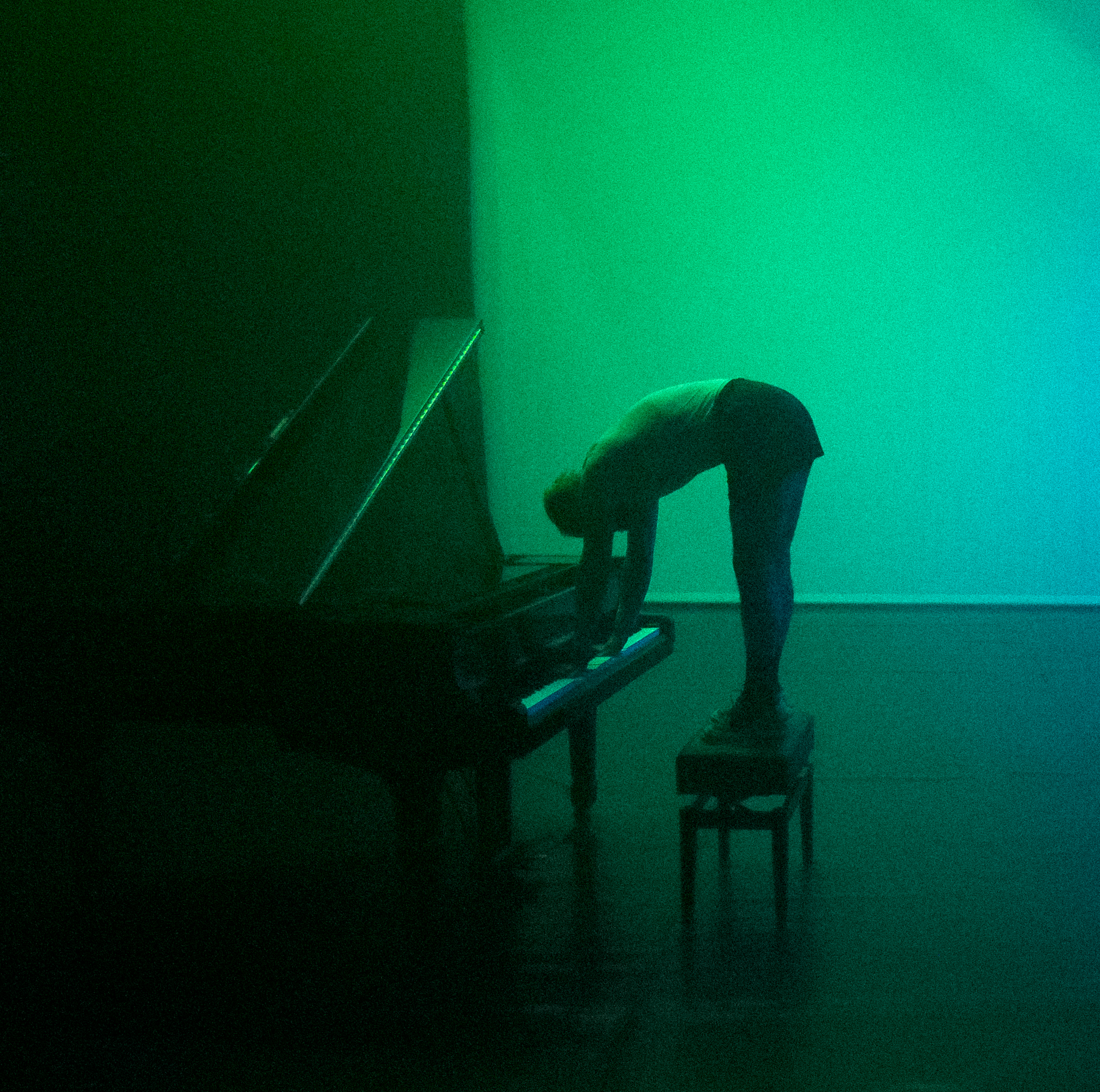 Óscar Bueno standing on the piano bench while playing it under a green light